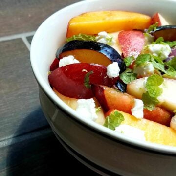 A bowl of delicious fruit salad featuring fresh stone fruits, goat cheese, and mint.