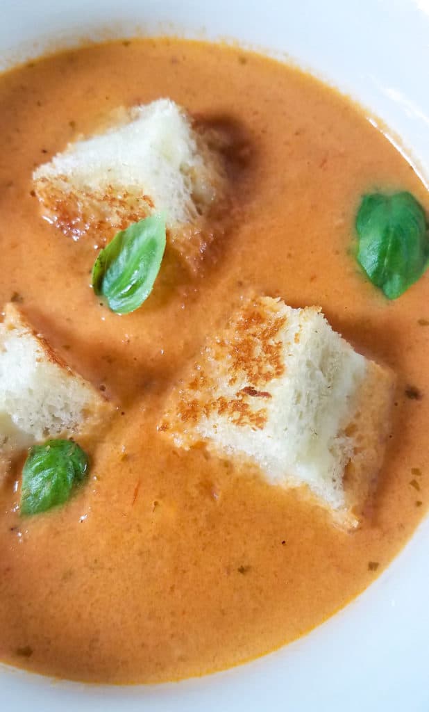 A vertical close up of creamy tomato bisque with three grilled cheese croutons.
