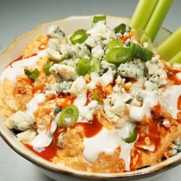 A bowl of Buffalo chicken dip with two celery stalks.