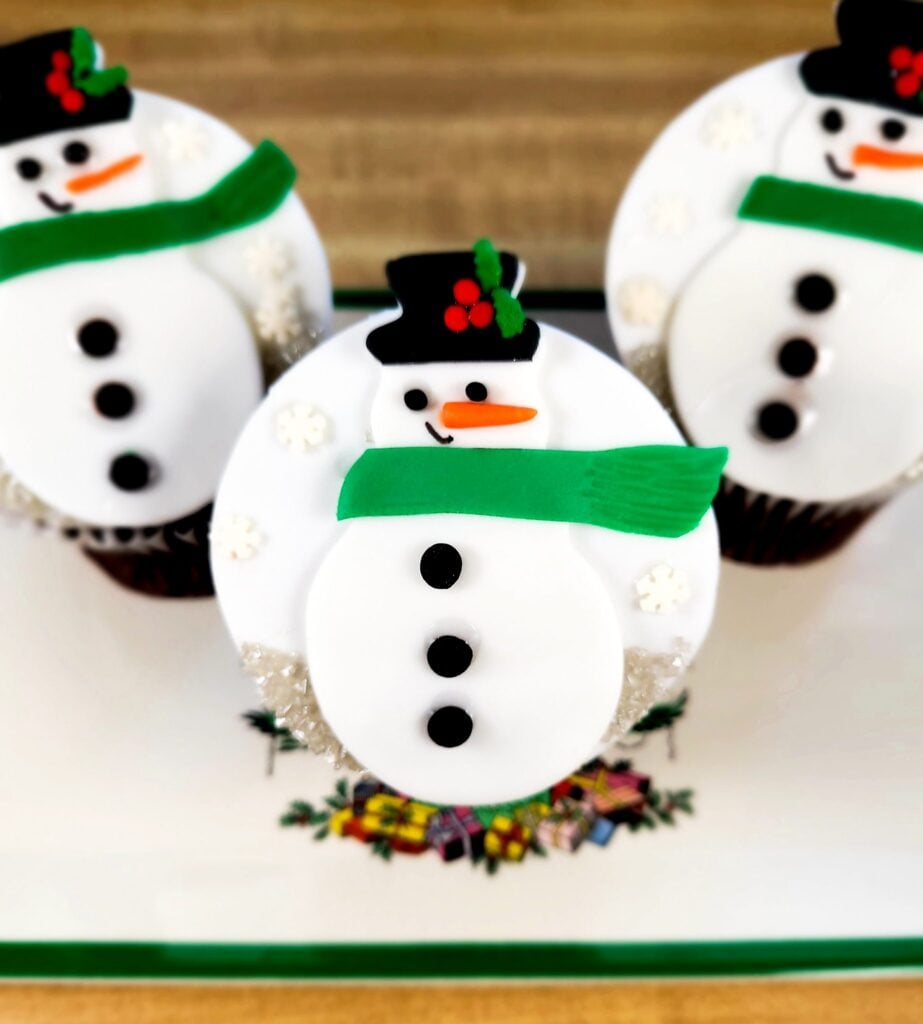 Three fondant snowman cupcake toppers on three chocolate cupcakes.