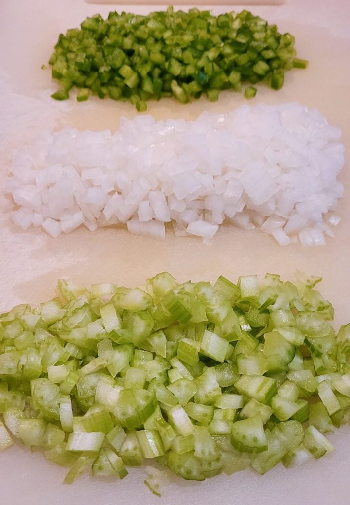 The Holy Trinity: celery, onion, and green bell pepper, finely chopped on a cutting board.