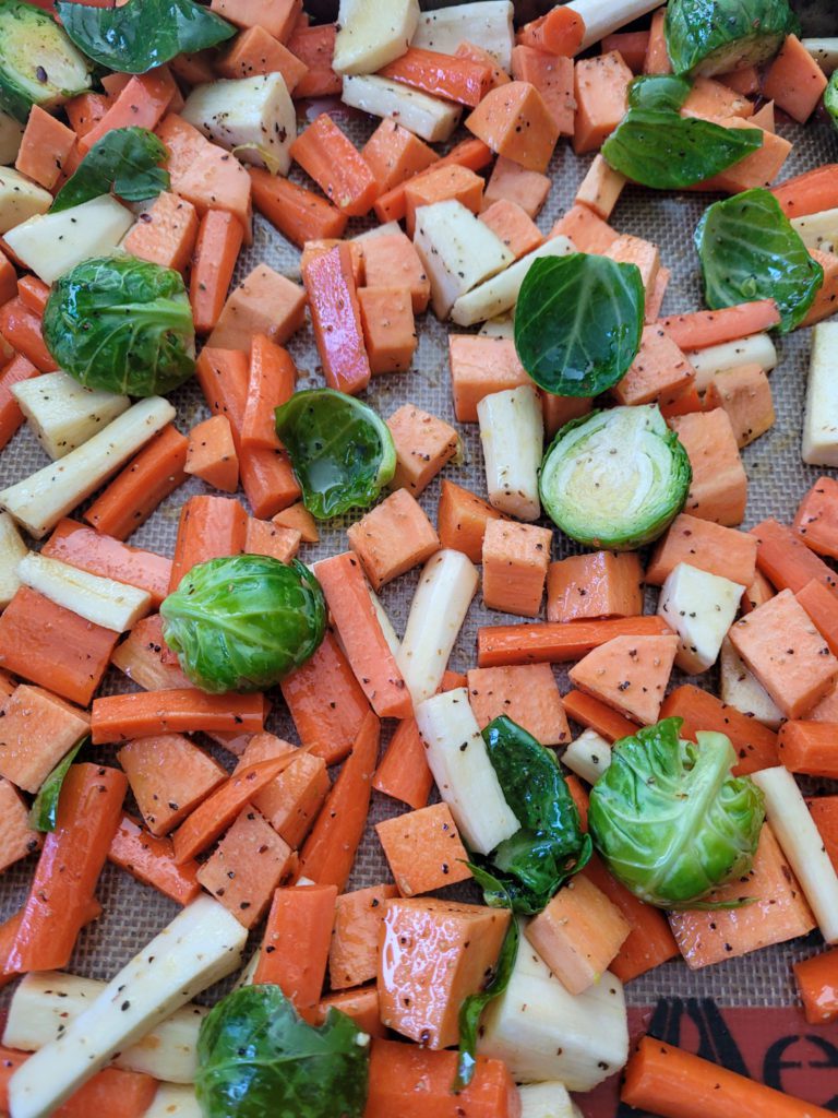 A sheet tray of raw carrots, parsnips, Brussels sprouts, and sweet potatoes.