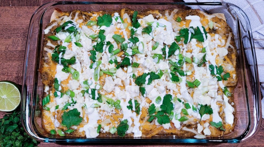 A casserole dish filled with chicken enchiladas with a roasted tomatillo sauce.