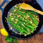 A skillet with vibrant green asparagus amandine with lemon and parsley.