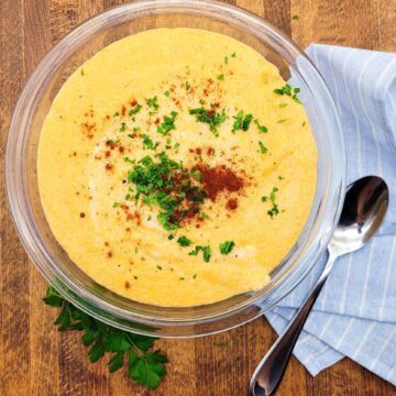 A bowl of smoked gouda cheese grits sprinkled with parsley and smoked paprika.