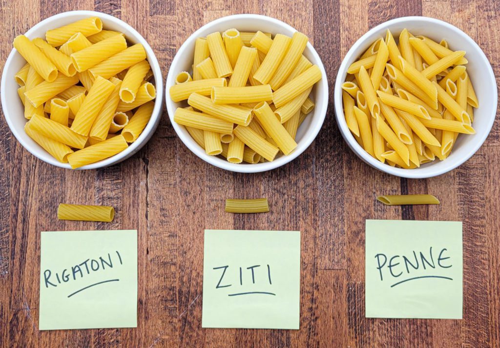 Rigatoni vs. ziti vs. penne - Rigatoni, ziti, and penne pasta in bowls side by side for comparison.