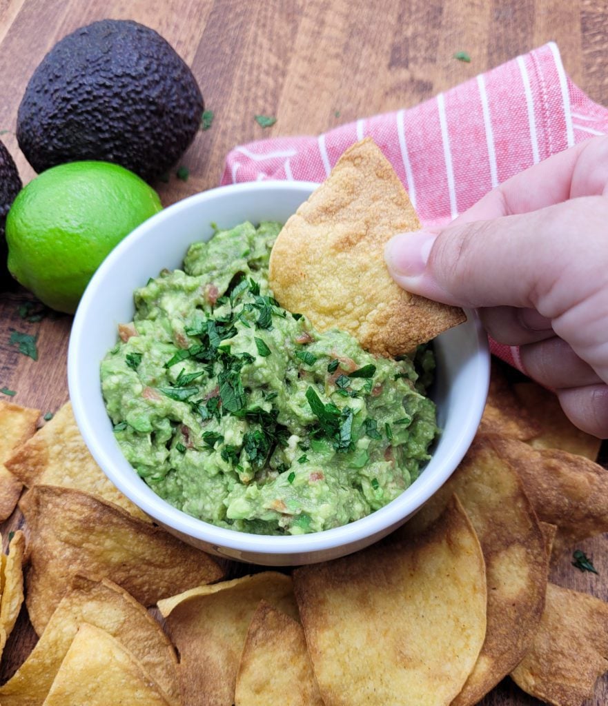 A hand dipping a chip into 4 ingredient guacamole