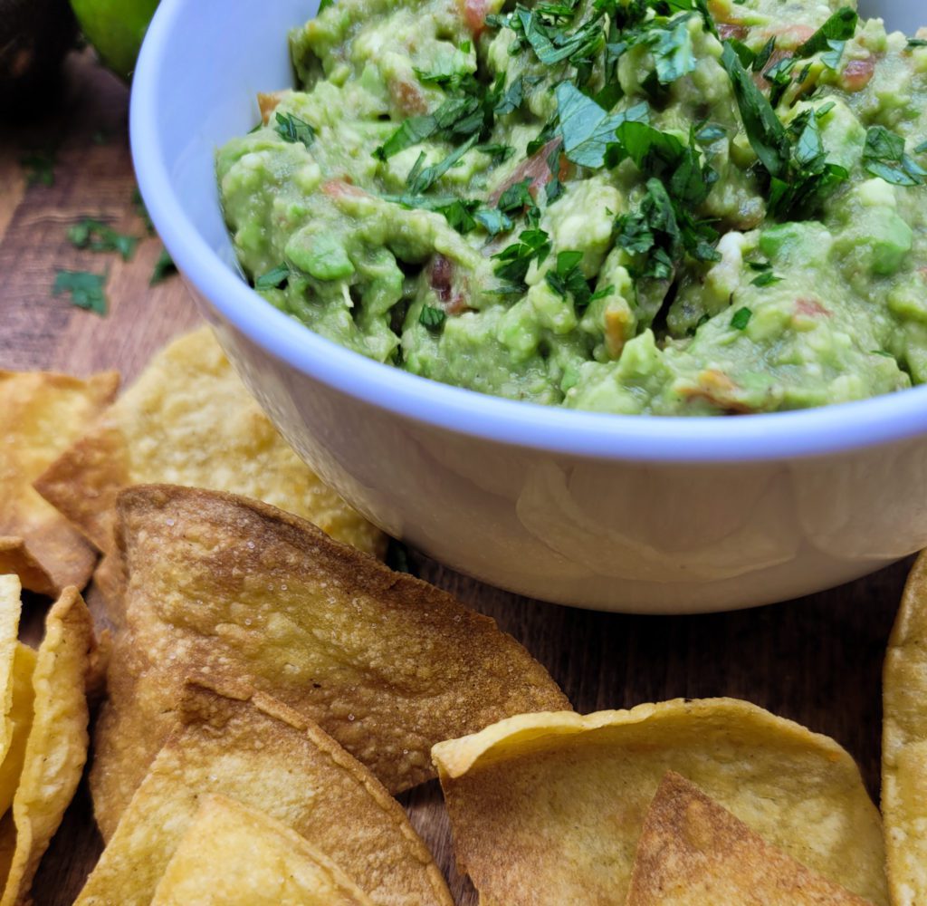 Side view of 4 ingredient guacamole in a white bowl with chips