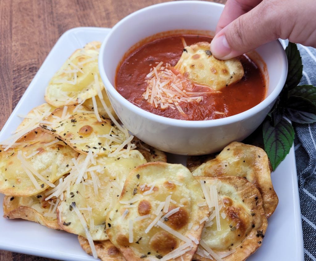 Hand dipping air fried ravioli into marinara sauce