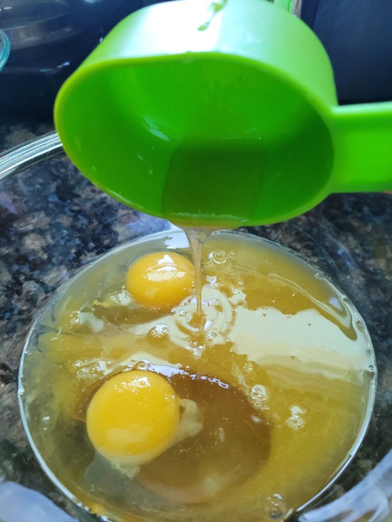 Two eggs, honey and orange juice in a clear mixing bowl