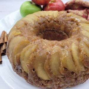 Apple Upside Down Bundt Cake on a white plate with apples and cinnamon sticks and a fall napkin