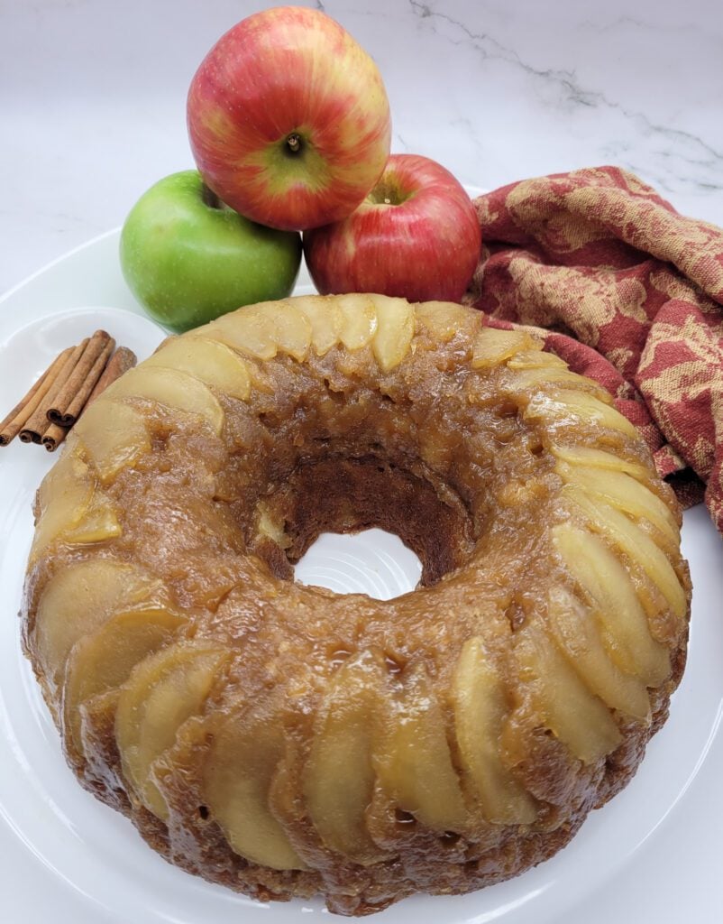 Apple Upside Down Bundt Cake on a white plate with apples and cinnamon sticks and a fall napkin