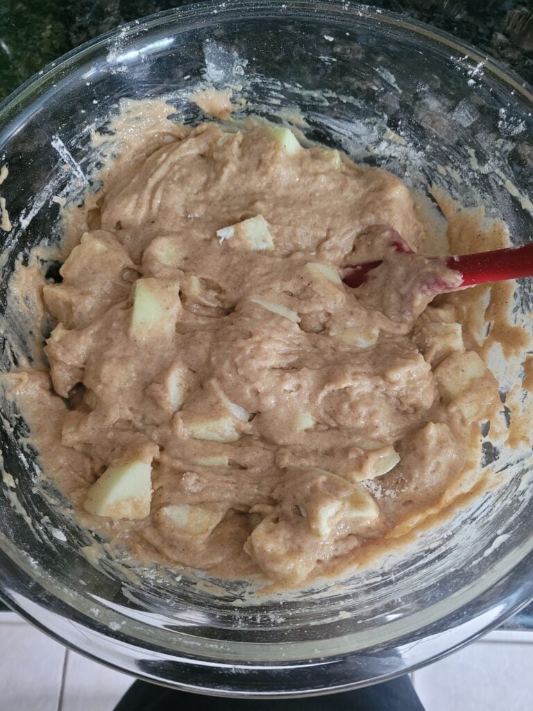 Red spatula mixing apples into cake batter for apple upside down bundt cake