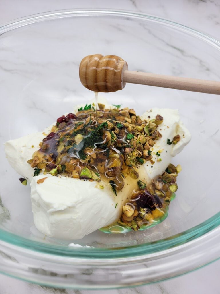 Adding honey to cheese, cranberries, pistachios, and parsley in preparation to make a Cranberry Pistachio Cheese Log