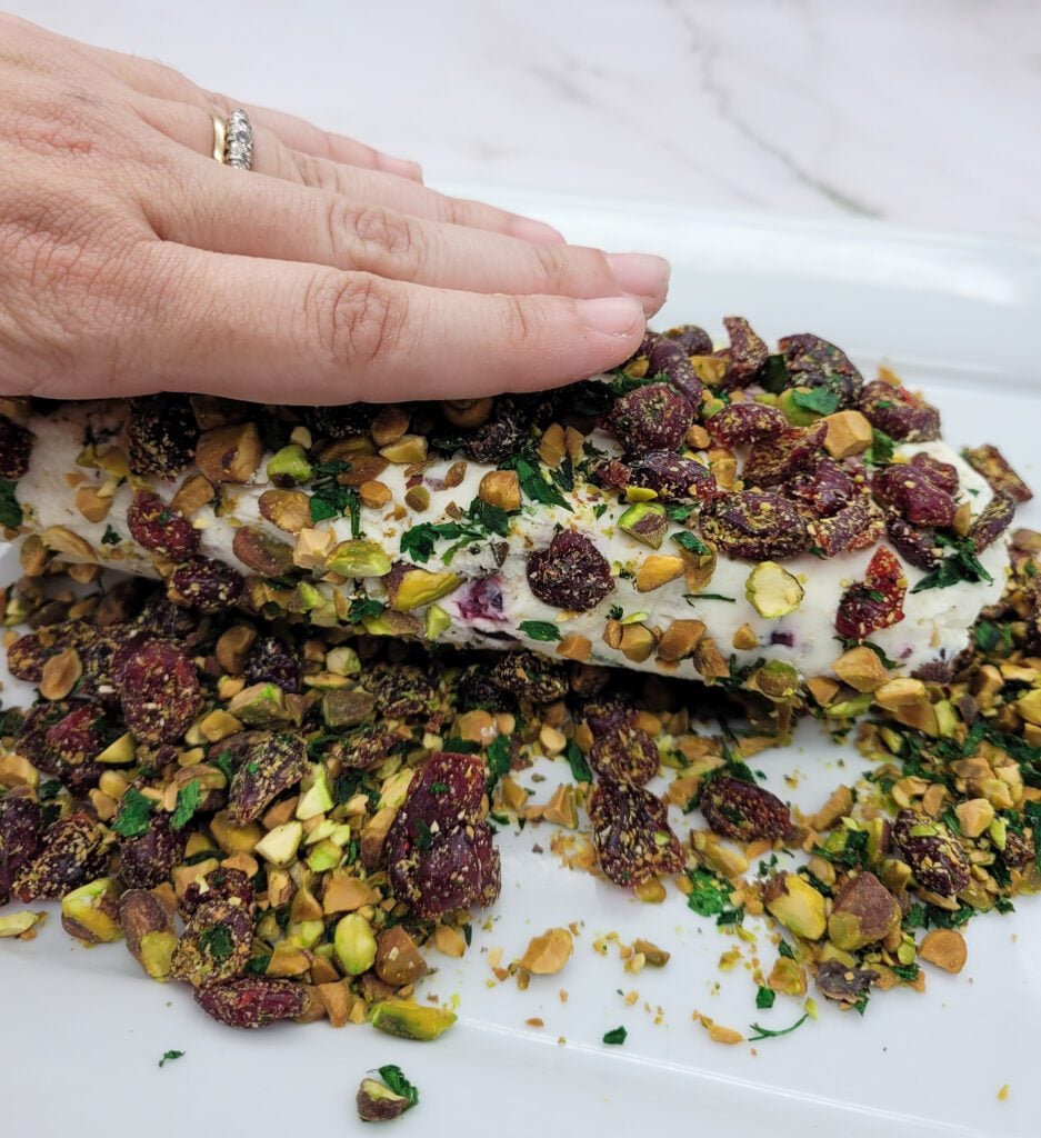 Coating Cranberry Pistachio Cheese Log with chopped pistachios, cranberries, and parsley