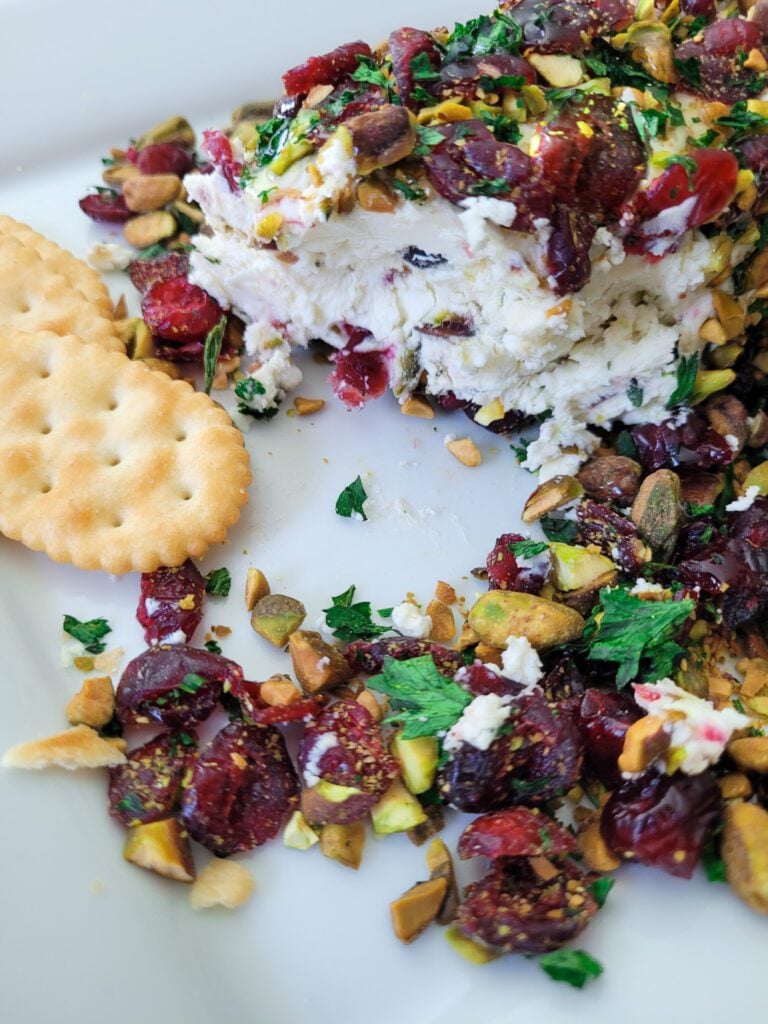 A partially eaten Cranberry Pistachio Cheese Log with two butter crackers