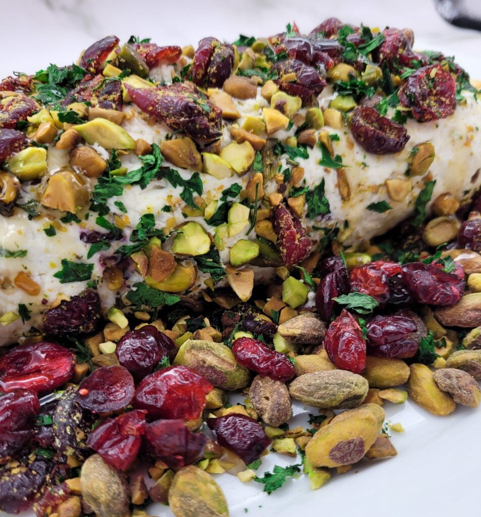 A close up of a Cranberry Pistachio Cheese Log on a white platter