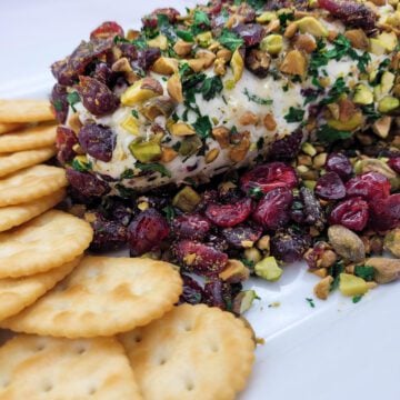 A diagonal view of a Cranberry Pistachio Cheese Log on a white platter with butter crackers