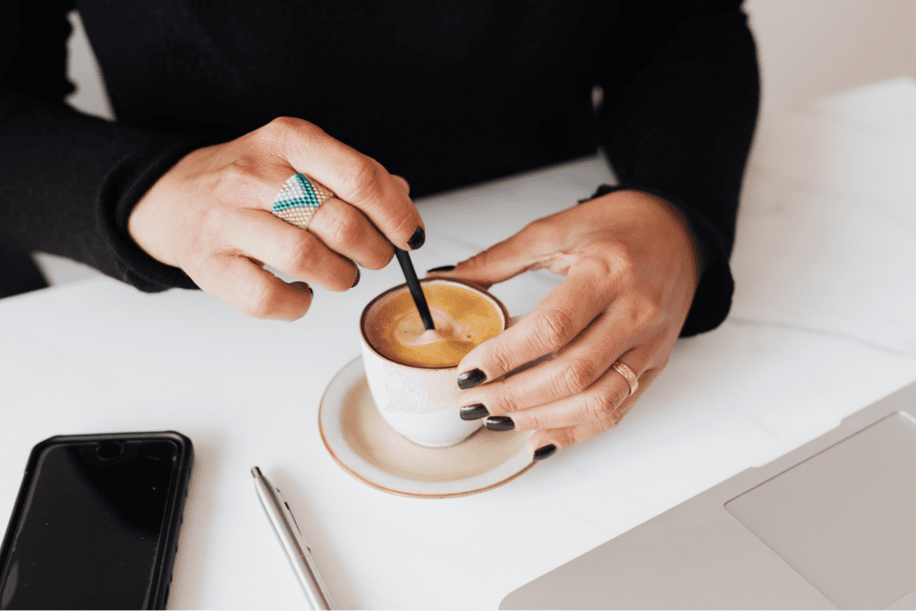 A woman's hands stirring a small white mug of espresso