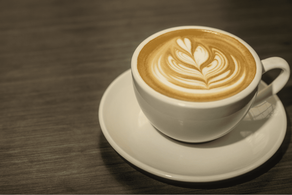 A latte with a leaf design in a white mug on a white saucer