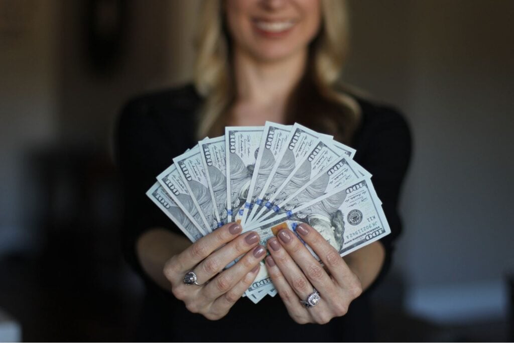 A woman holding up fanned out one hundred dollar bills