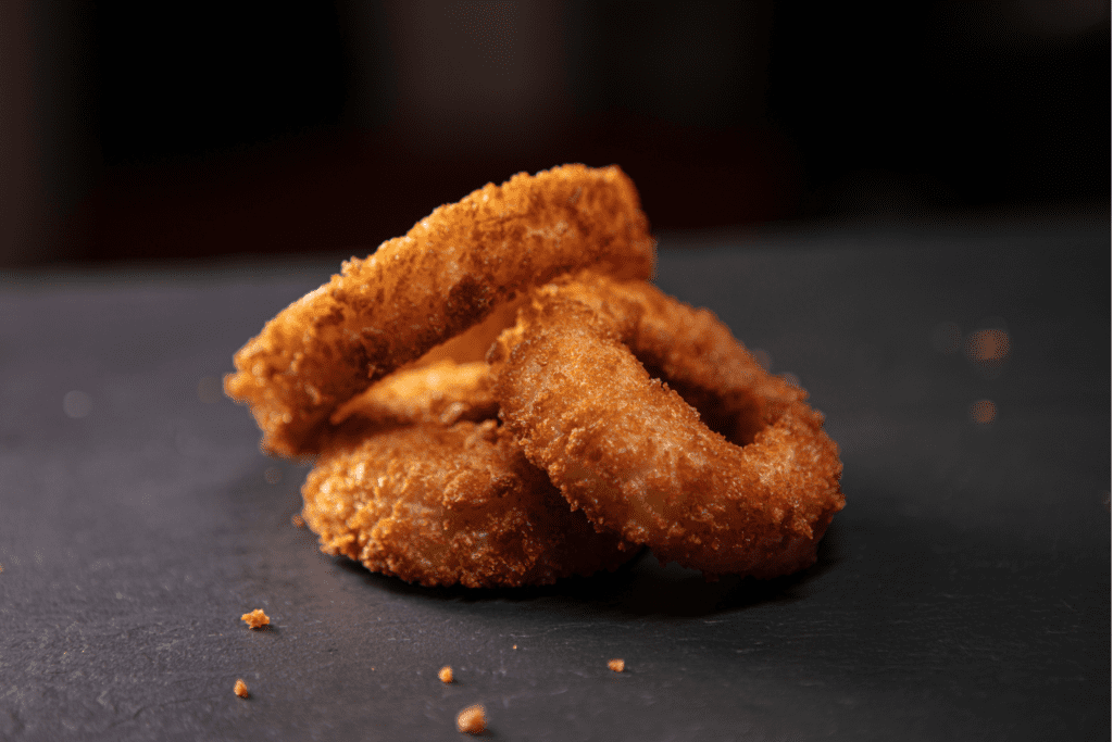 A pile of three onion rings against a dark background