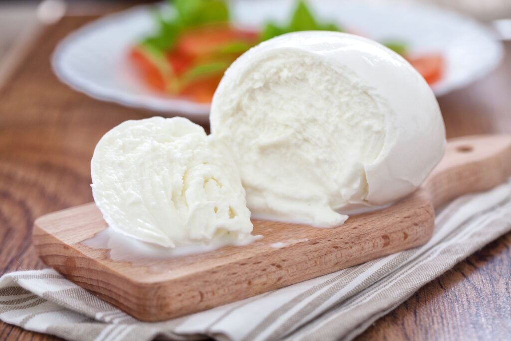 A close up of a burrata cheese ball on a small cutting board